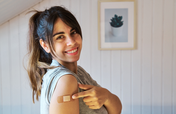 Woman proudly pointing to a band aid on her arm where she was vaccinated against COVID-19