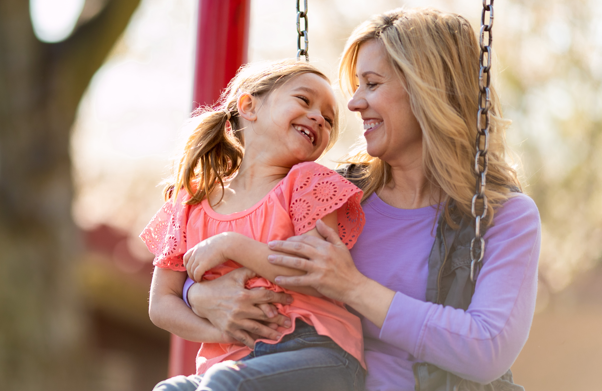 A mother sitting in a swing set holding her daughter smiling