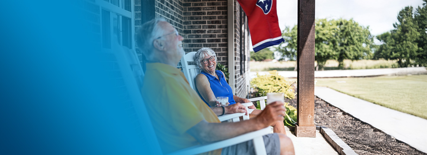 An older couple conversing and smiling while sitting on their front porch in rocking chairs. An older couple conversing and smiling while sitting on their front porch in rocking chairs.