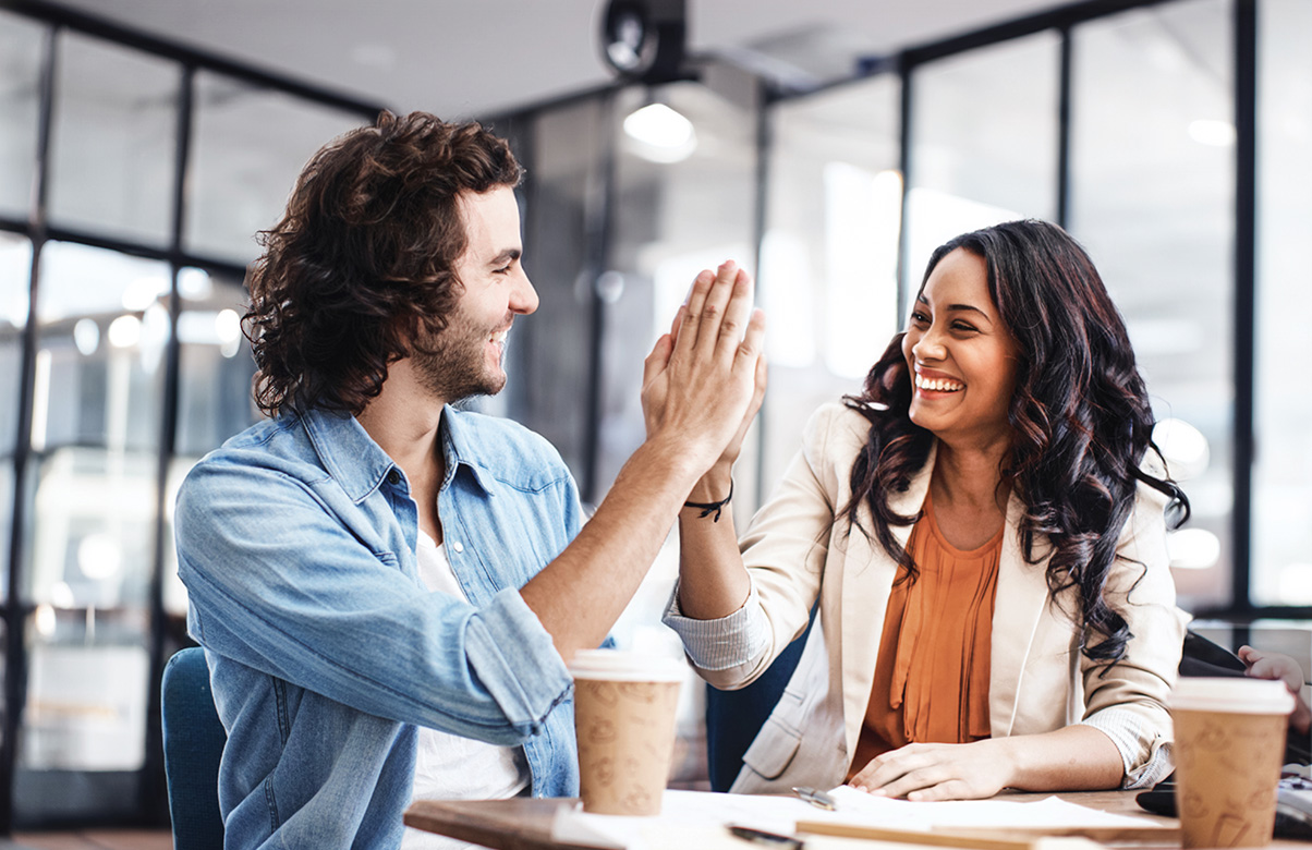 Two coworkers sitting together and giving each other a high five