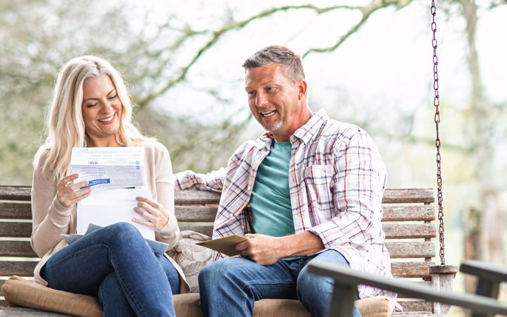 a man and woman are sitting outside on their porch reviewing their plan benefits