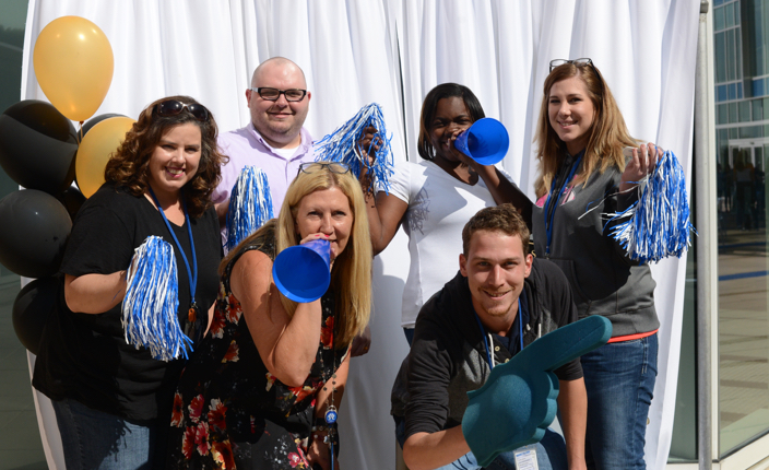 6 people celebrating serving their communities with blue and white blow horns and pom poms