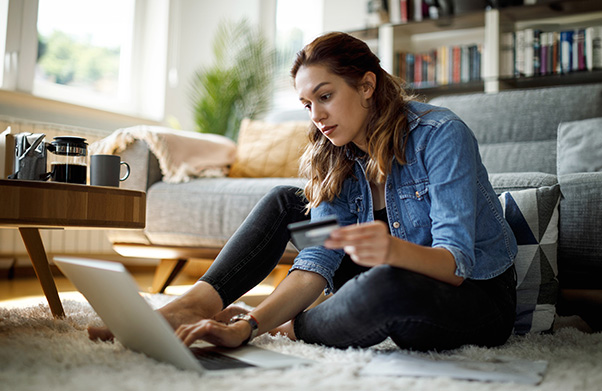 Woman sitting on rug with her computer and credit card making an online purchase