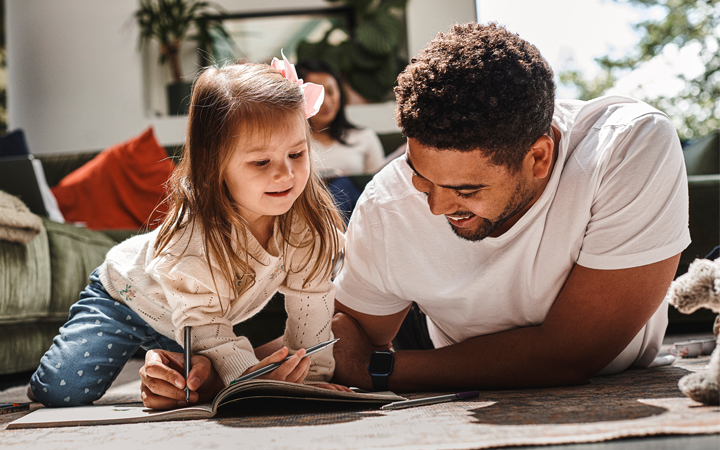 Father and daughter on the floor drawing in a notebook