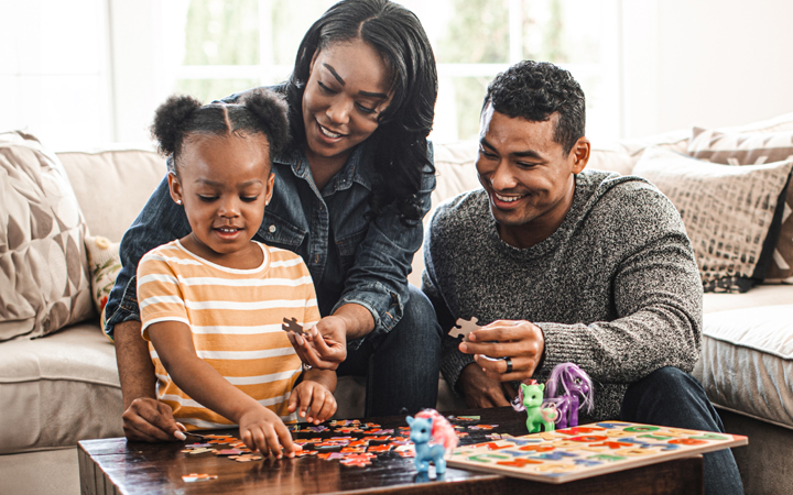 Small family of mother, father and daughter playing in their living room with puzzles