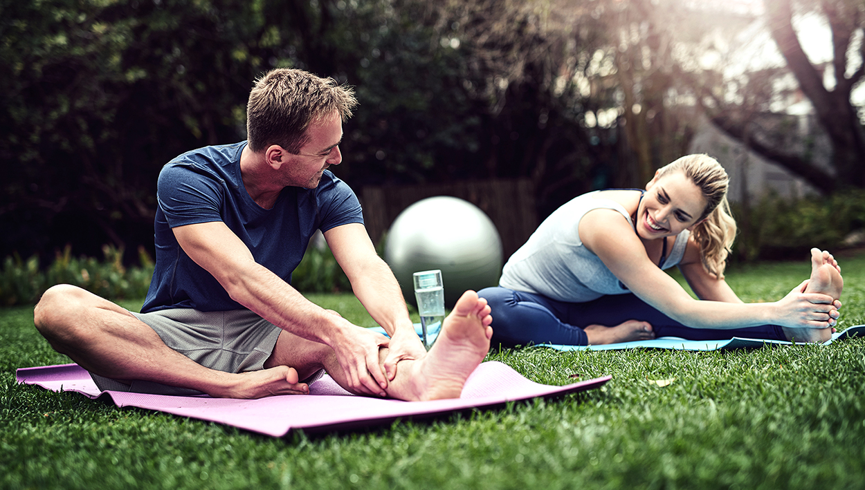 Two young adults stretching on yoga mats outside