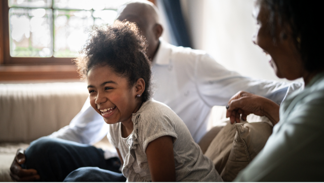 Young child laughing at her parents while sitting on couch