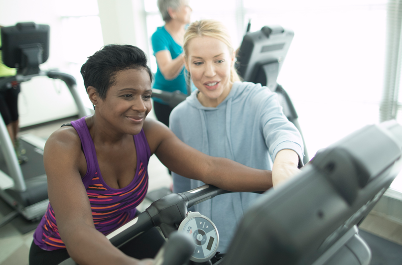 A woman assisting a lady on exercise equipment