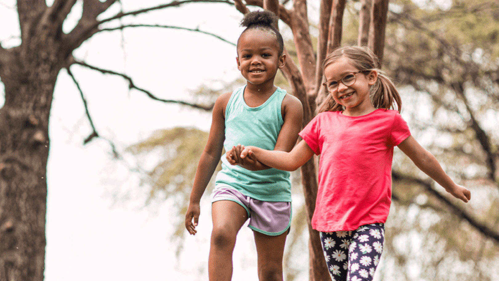 Two young girls holding hands and walking outside